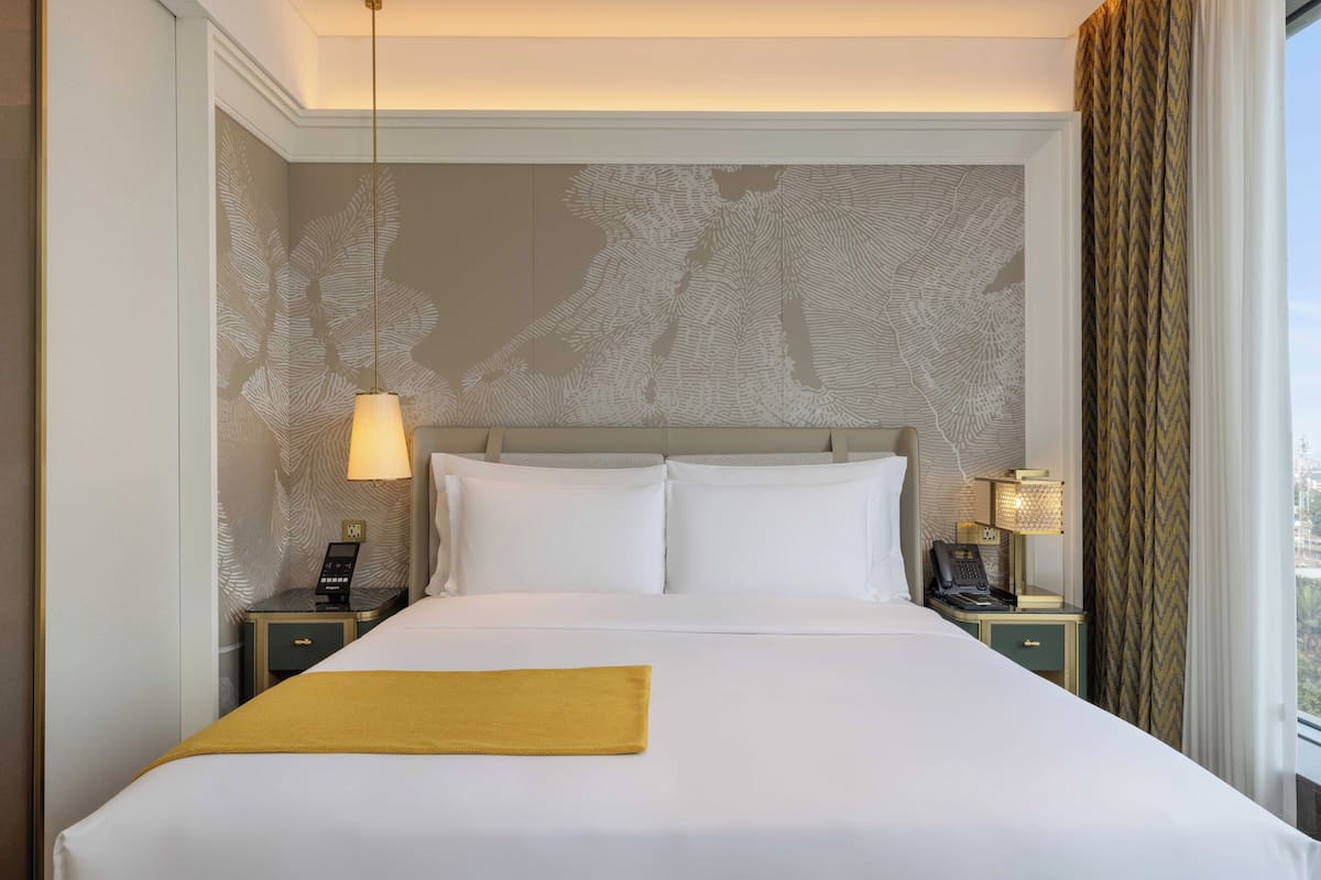 A hotel room with a large bed, two bedside tables, a telephone, and a lamp.