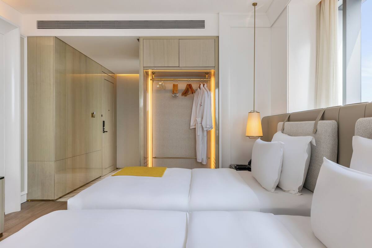 A modern hotel room with a large bed, a walk-in closet, and a view of the city.