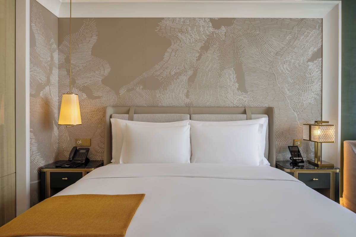 A hotel room with a large bed, two bedside tables, a telephone, and a lamp.