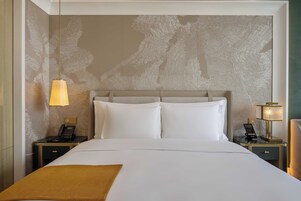 Una habitación de hotel con una cama grande, dos mesitas de noche, un teléfono y una lámpara.