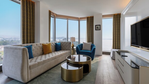 Una habitación de hotel moderna con sofá, sillón, una mesa redonda de centro y televisor.