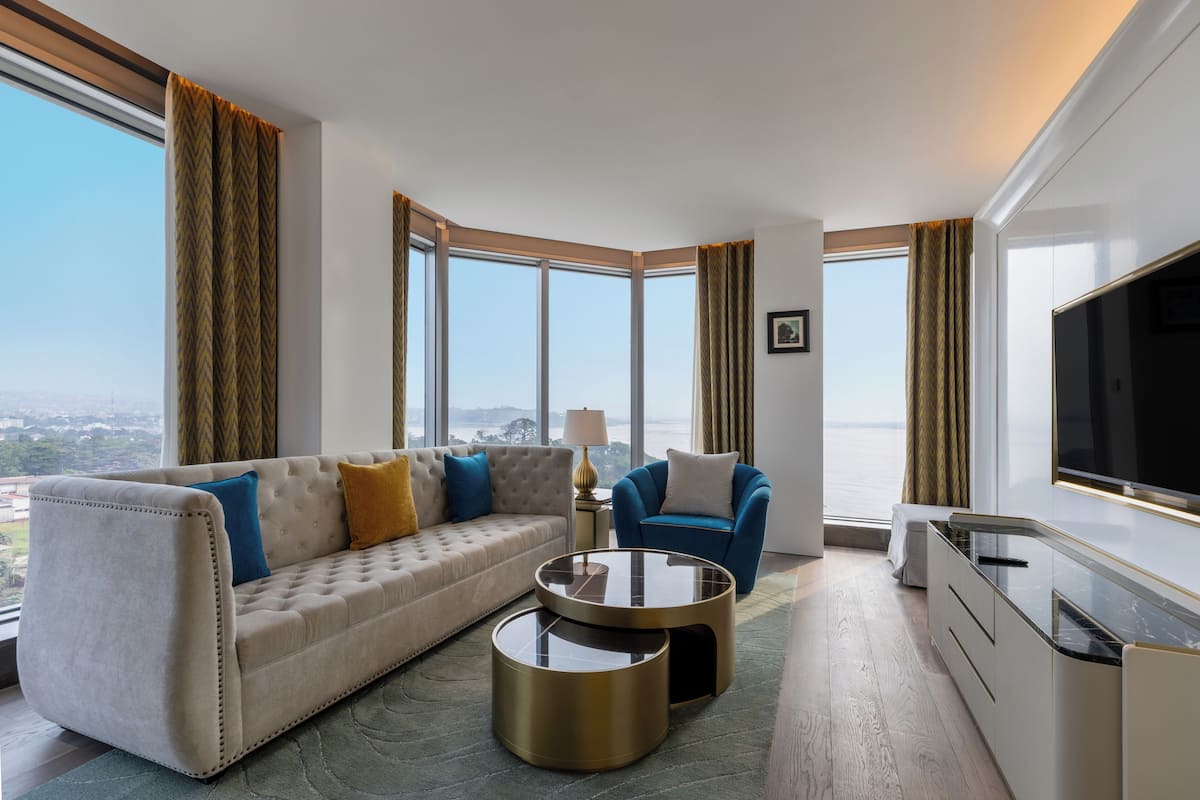 A modern hotel room with a sofa, armchair, round coffee table, and a TV.