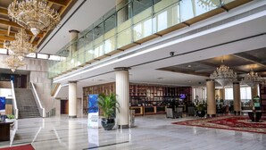 Un vestíbulo espacioso con techo alto, grandes candelabros, una imponente escalera y una zona de recepción con alfombra roja.