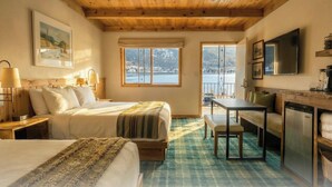 A cozy bedroom with a wooden ceiling, a bed, a desk, and a view of a lake. - Western Riviera Lakeside Lodging (Grand Lake)