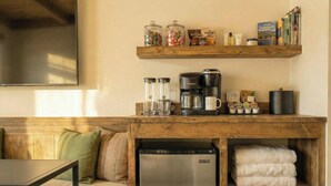 A cozy living area with a wooden bench, a coffee station, and a bookshelf with books and a local guidebook. - Western Riviera Lakeside Lodging (Grand Lake)