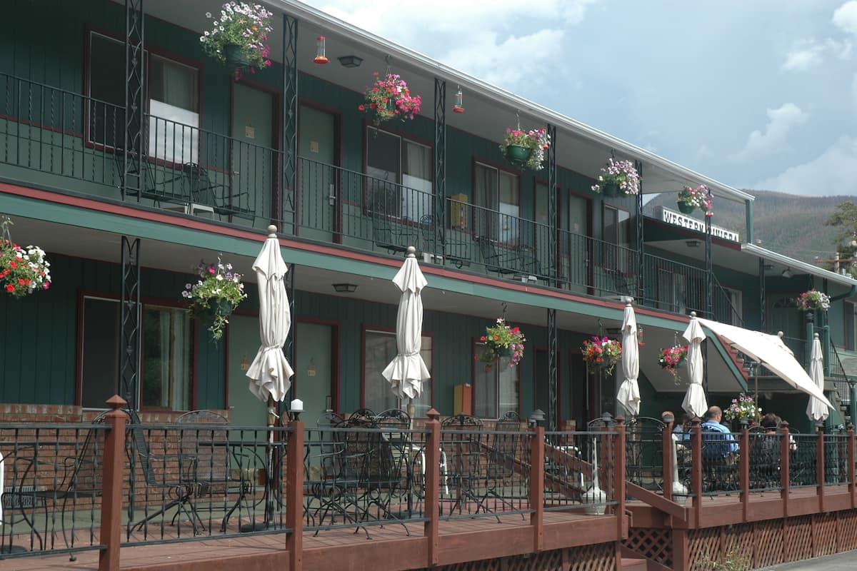 Un edificio de dos pisos con balcón, asientos exteriores y cestas de flores colgantes.