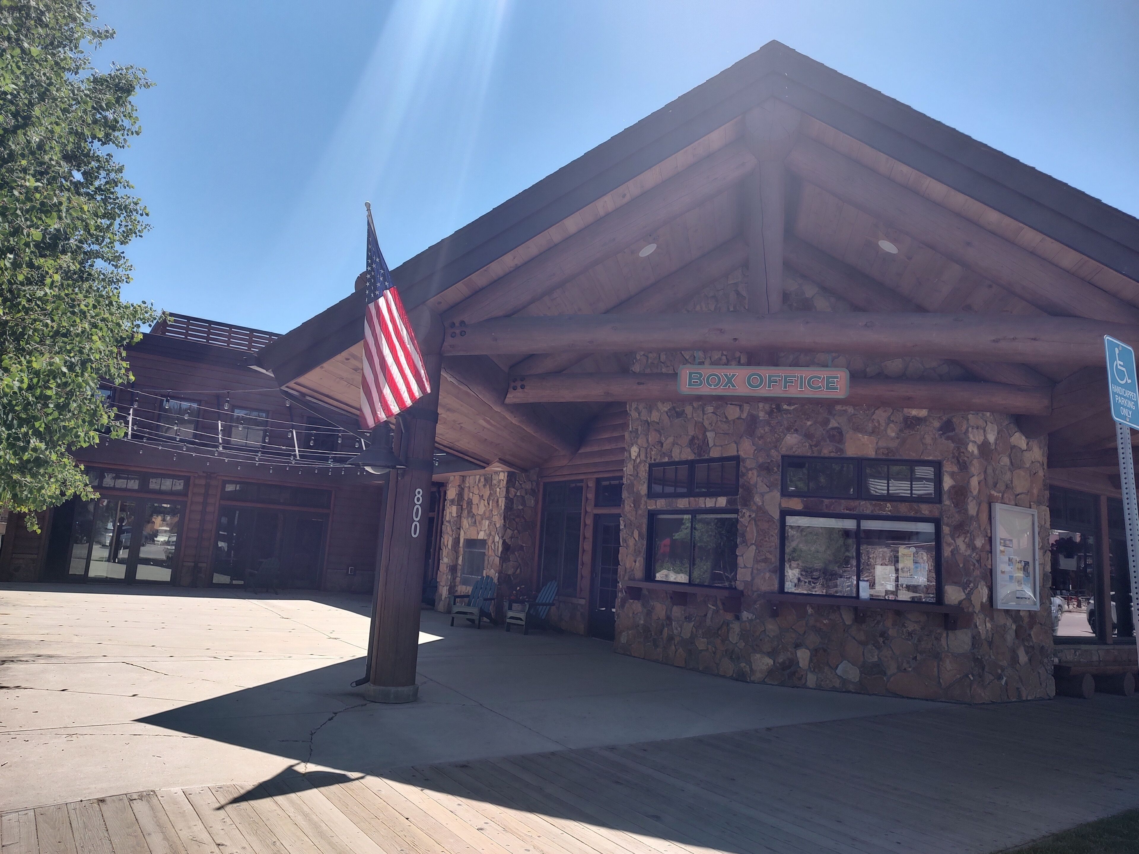 A wooden building with a stone facade, labeled "Box Office," and an American flag.
