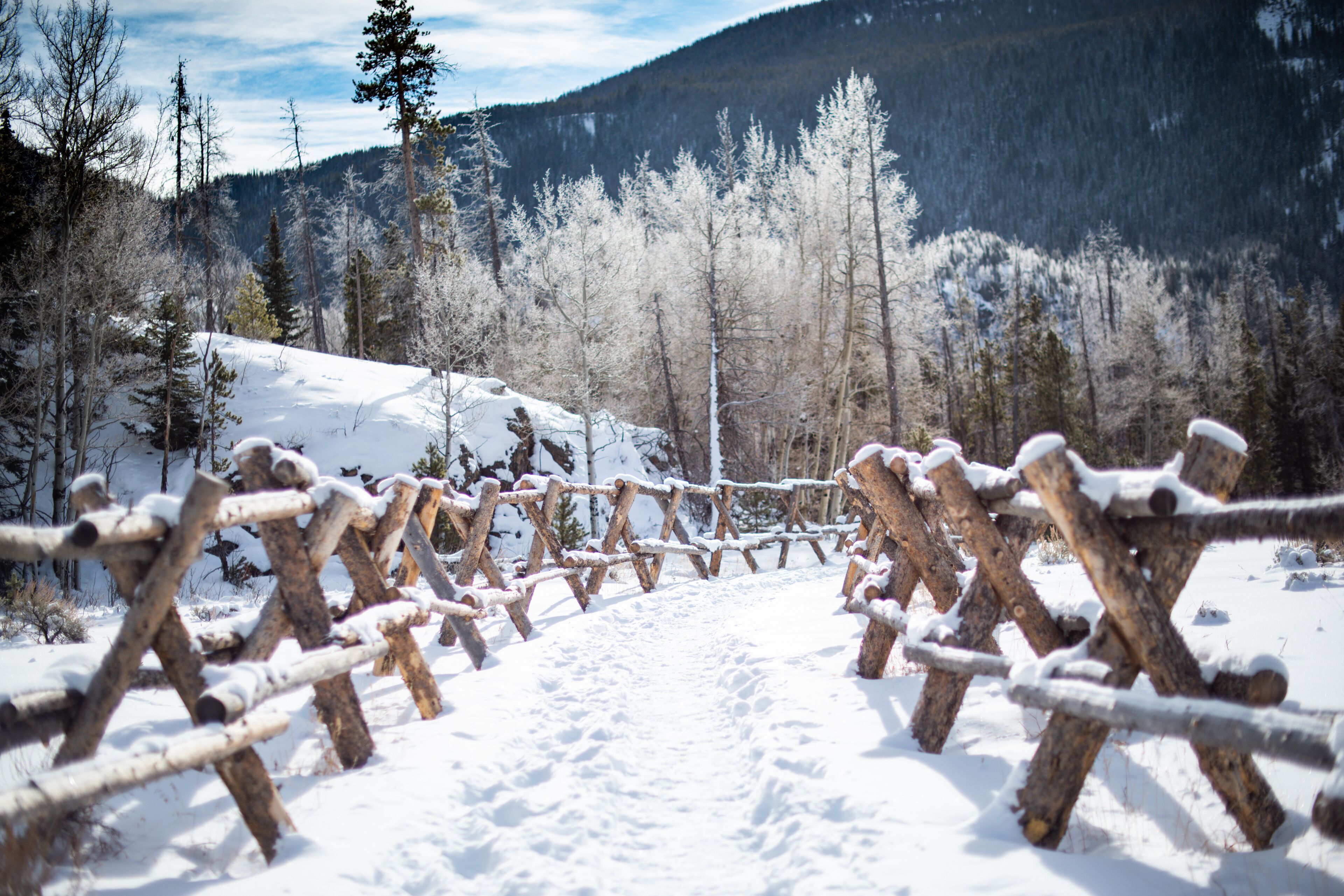 A snow-covered wooden fence in a mountainous area.