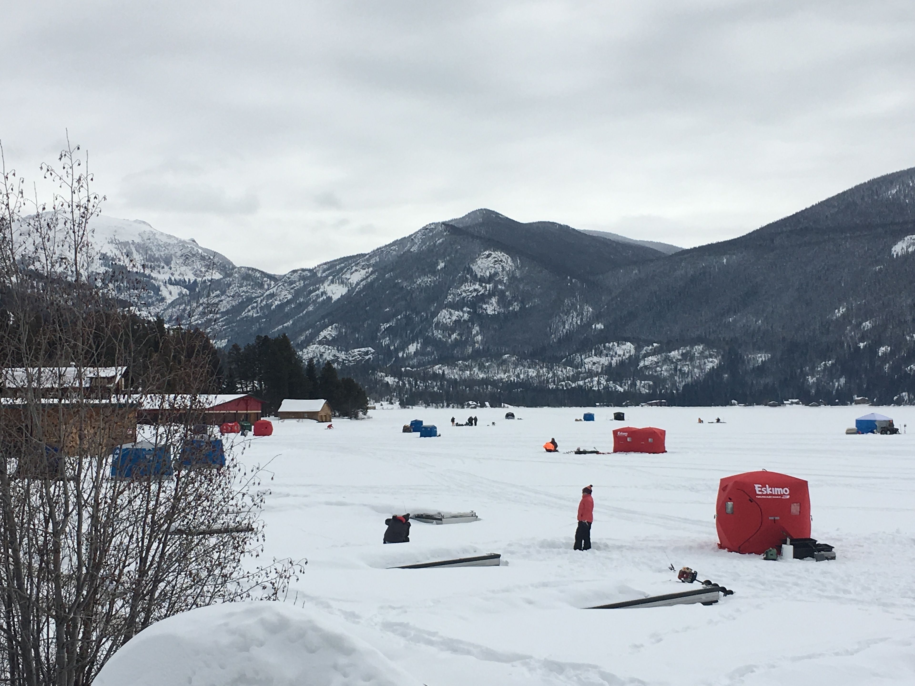Un paysage enneigé avec des tentes et un petit bâtiment, probablement un chalet, entouré de montagnes.