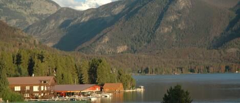 A lakeside cabin with a dock, surrounded by mountains and dense forest.