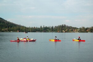 A calm lake with kayaks and canoes, surrounded by forested hills and distant buildings.