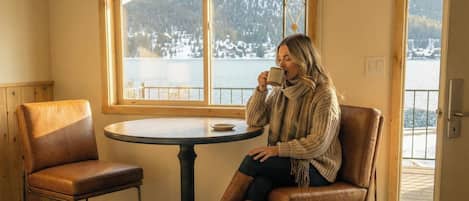 A woman sitting at a round table by a window with a view of a snowy landscape.