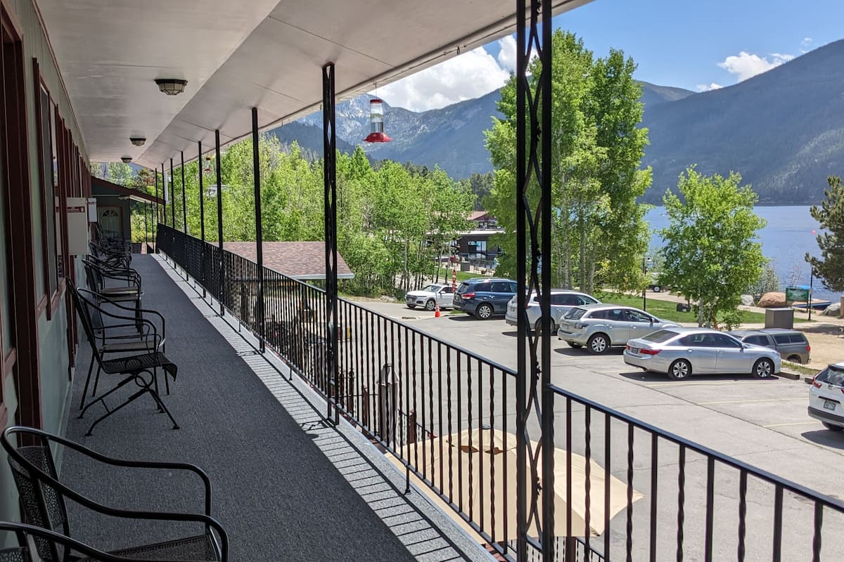 Un balcón con sillas, vista a un estacionamiento y un lago con montañas al fondo.