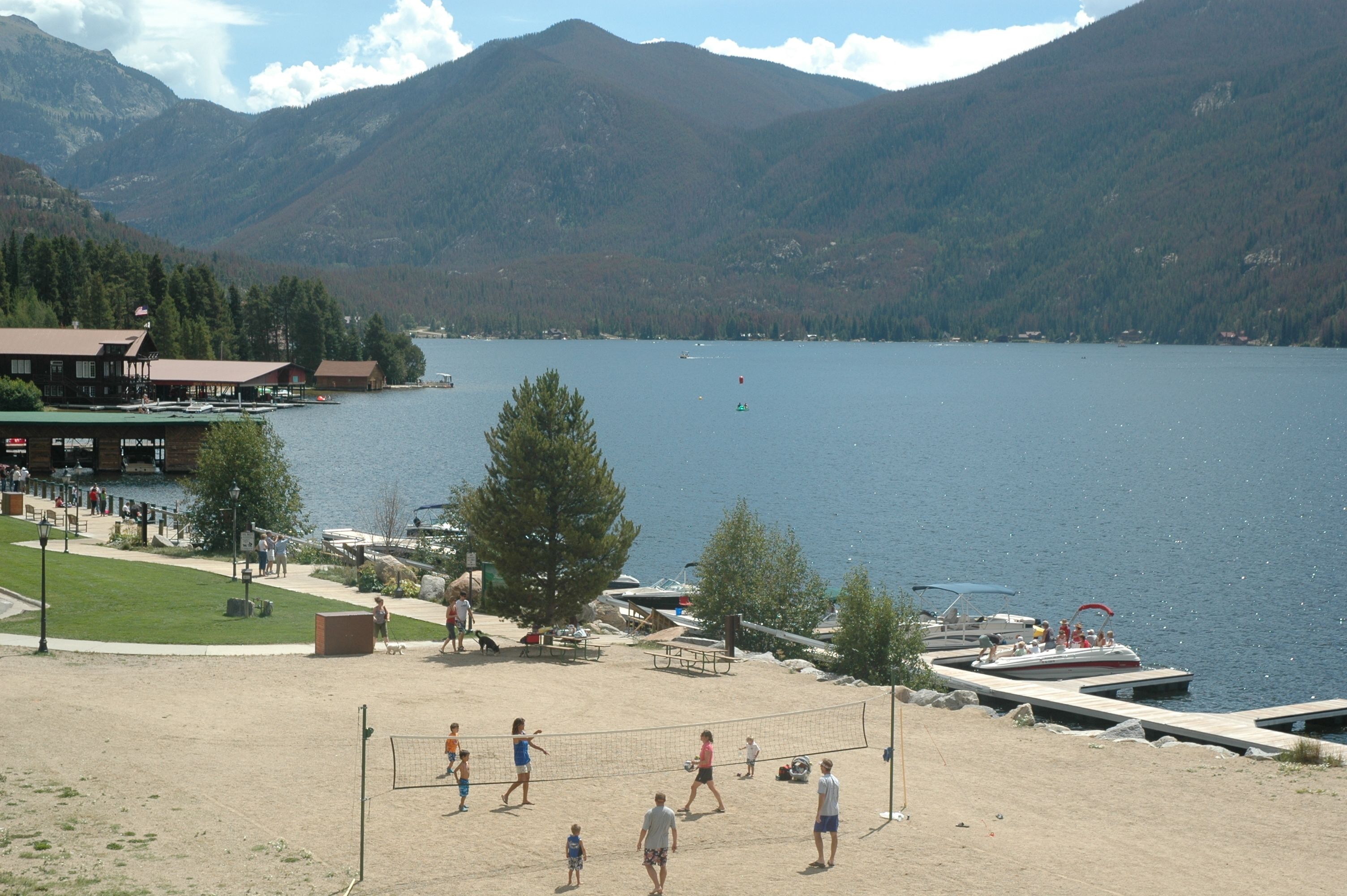 Una spiaggia sul lago con una rete da pallavolo, barche e un edificio con un molo.