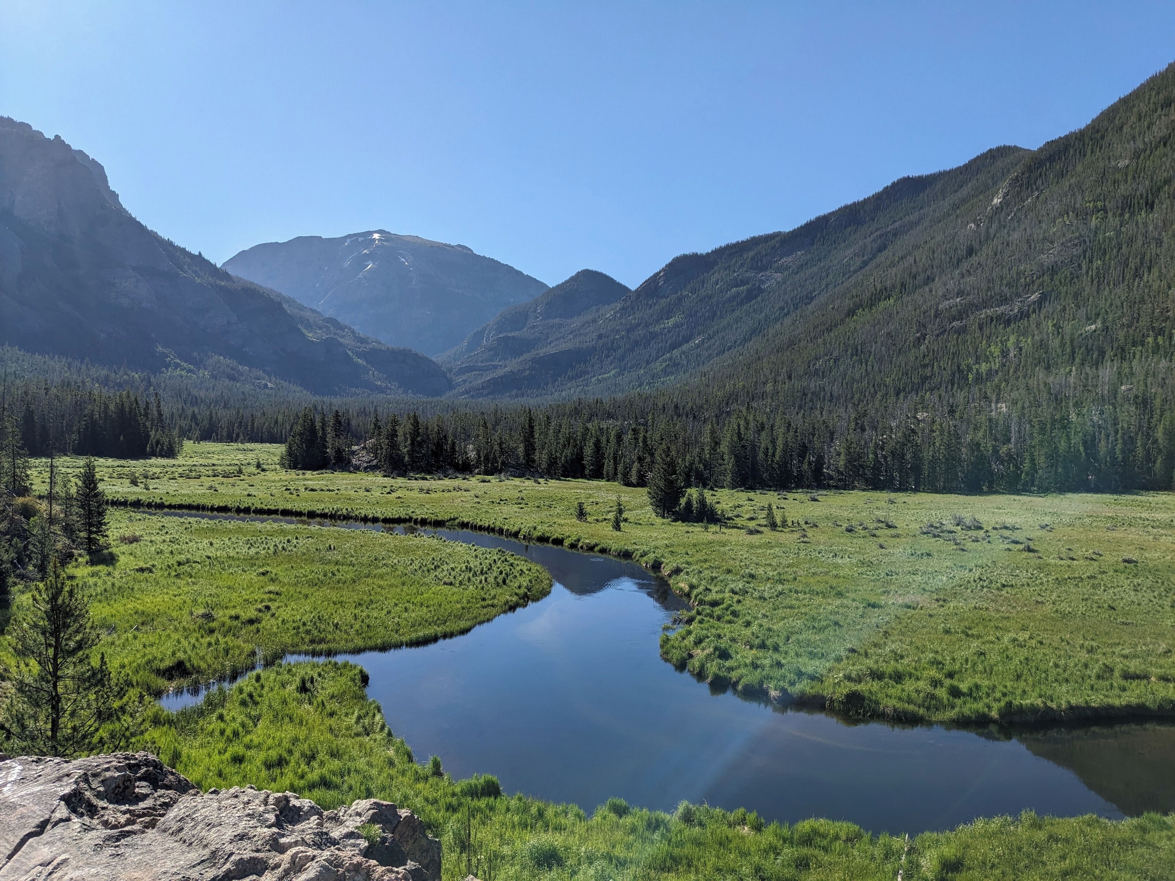 Un paisaje sereno con un río que serpentea por un valle, rodeado de bosques densos y montañas.