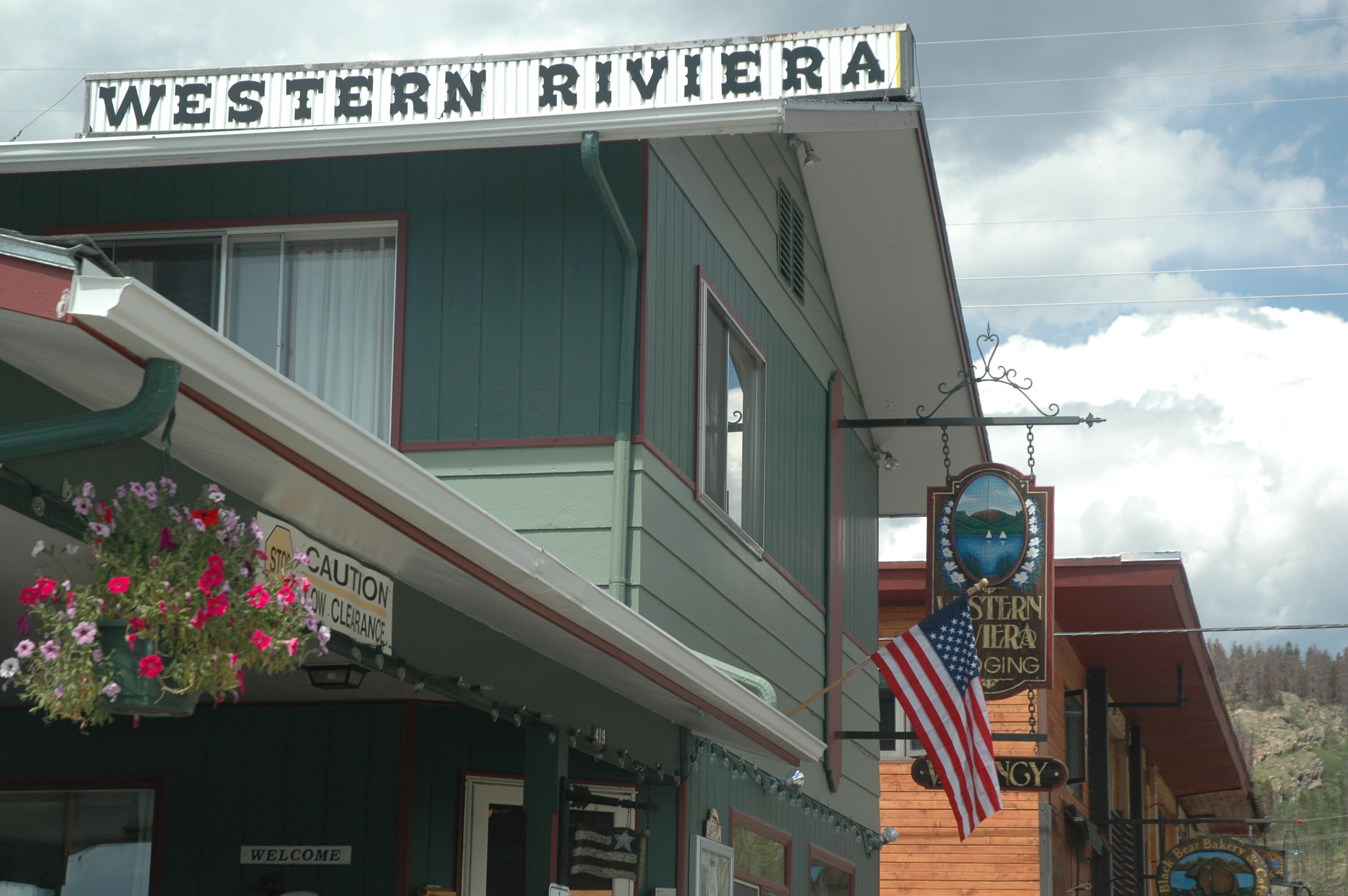 A Western Riviera building with a "Welcome" sign, a "Stay Caution" sign, and an American flag.