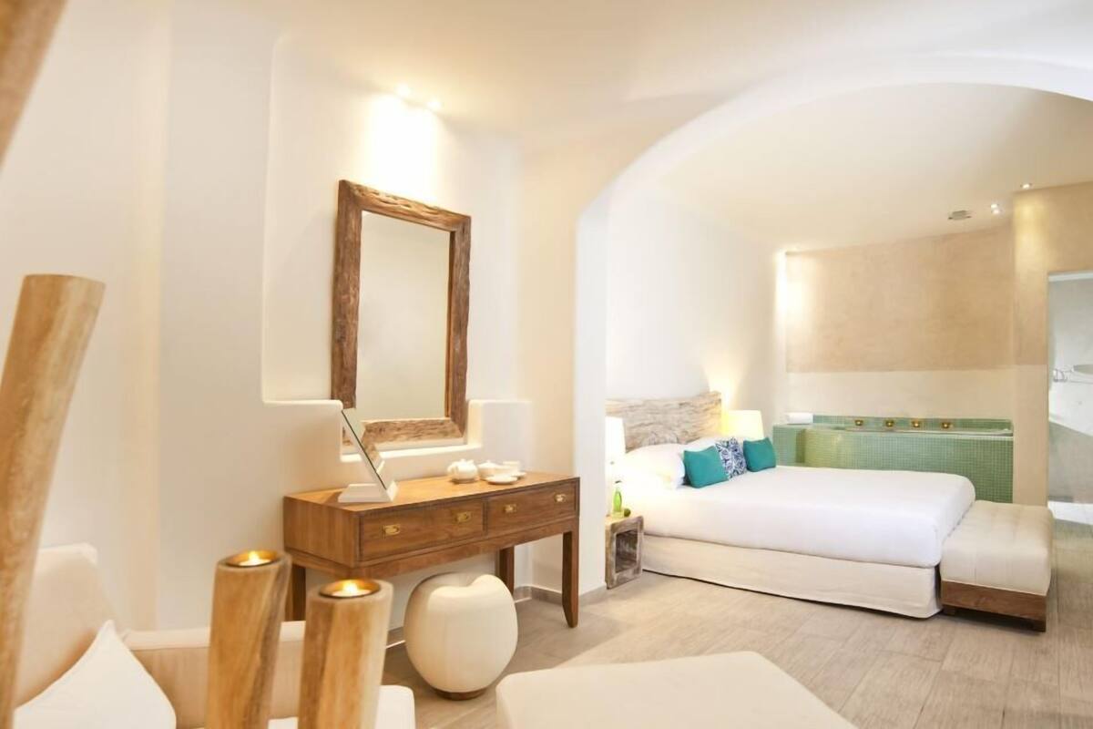 A modern bedroom with a large bed, a wooden dresser, a mirror, and a nightstand with a lamp.