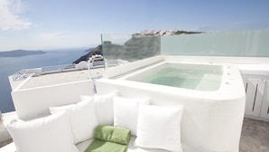 Una terraza en la azotea con jacuzzi, mobiliario blanco y vistas al mar y a los acantilados.