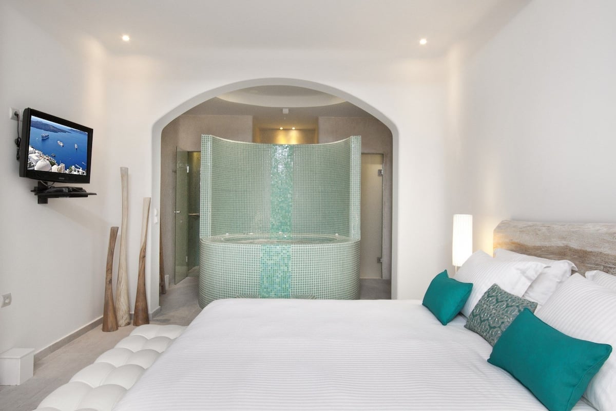 A modern hotel room with a large bed, a television on the wall, and a glass-enclosed shower area.