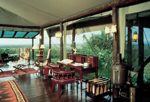 A room with a wooden table, chairs, a desk, and a large window with a view of the landscape.
