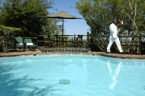 Piscina com deck de madeira, cadeiras de descanso e uma pessoa passando.