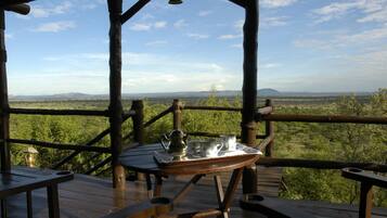 A wooden deck with a table set for tea, overlooking a scenic landscape.