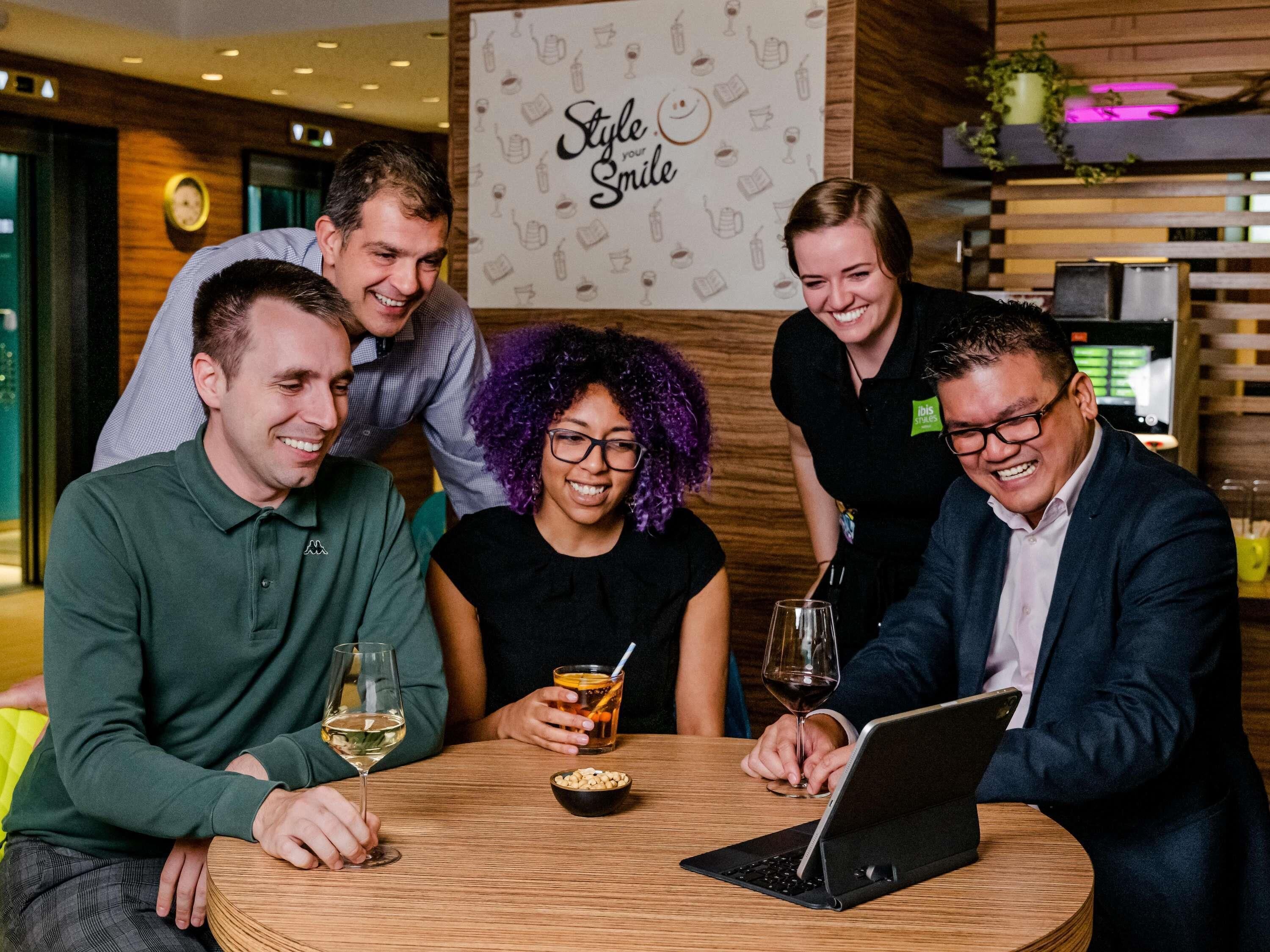 A group of people sitting around a wooden table in a modern indoor setting with a sign reading "Style your Smile".