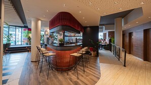 A modern bar area with a curved counter, bar stools, and a red accent wall. - Ibis Styles Wien City (Vienna)
