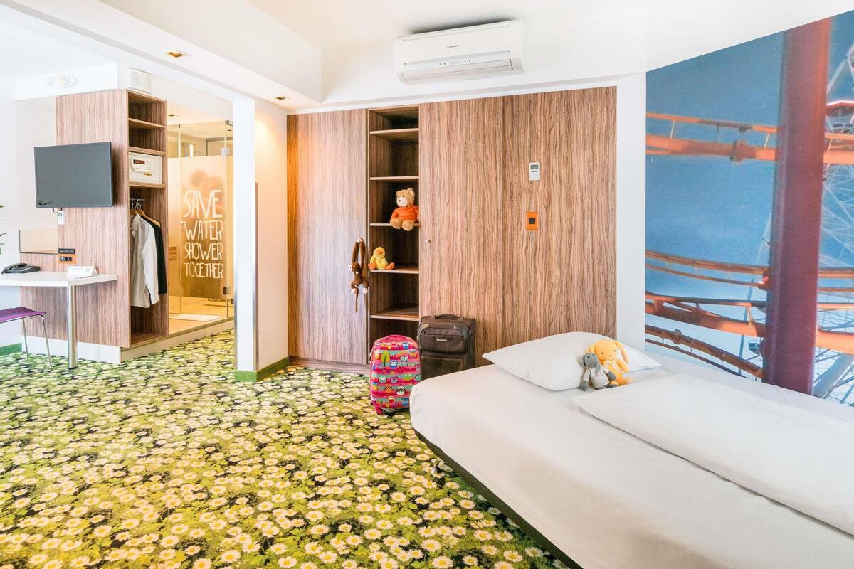 A hotel room with a bed, a desk, a wardrobe, and a large window with a view of a bridge.