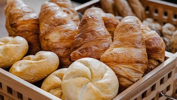 Una caja de madera llena de diferentes tipos de pan, incluyendo cruasanes y barras.
