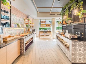 A modern buffet area with a variety of food options, wooden shelves, and decorative plants. - Ibis Styles Wien City (Vienna)