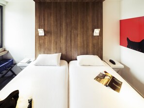 A hotel room with two beds, a wooden headboard, bedside tables with lamps, a red wall art, and a magazine on the bed. - Hotel ibis Styles Niort Poitou Charentes (Vouille)