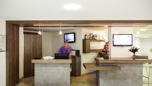 Un espace d’accueil comprenant un comptoir de réception en bois, un ordinateur, un téléviseur et un coin bar avec des bouteilles.