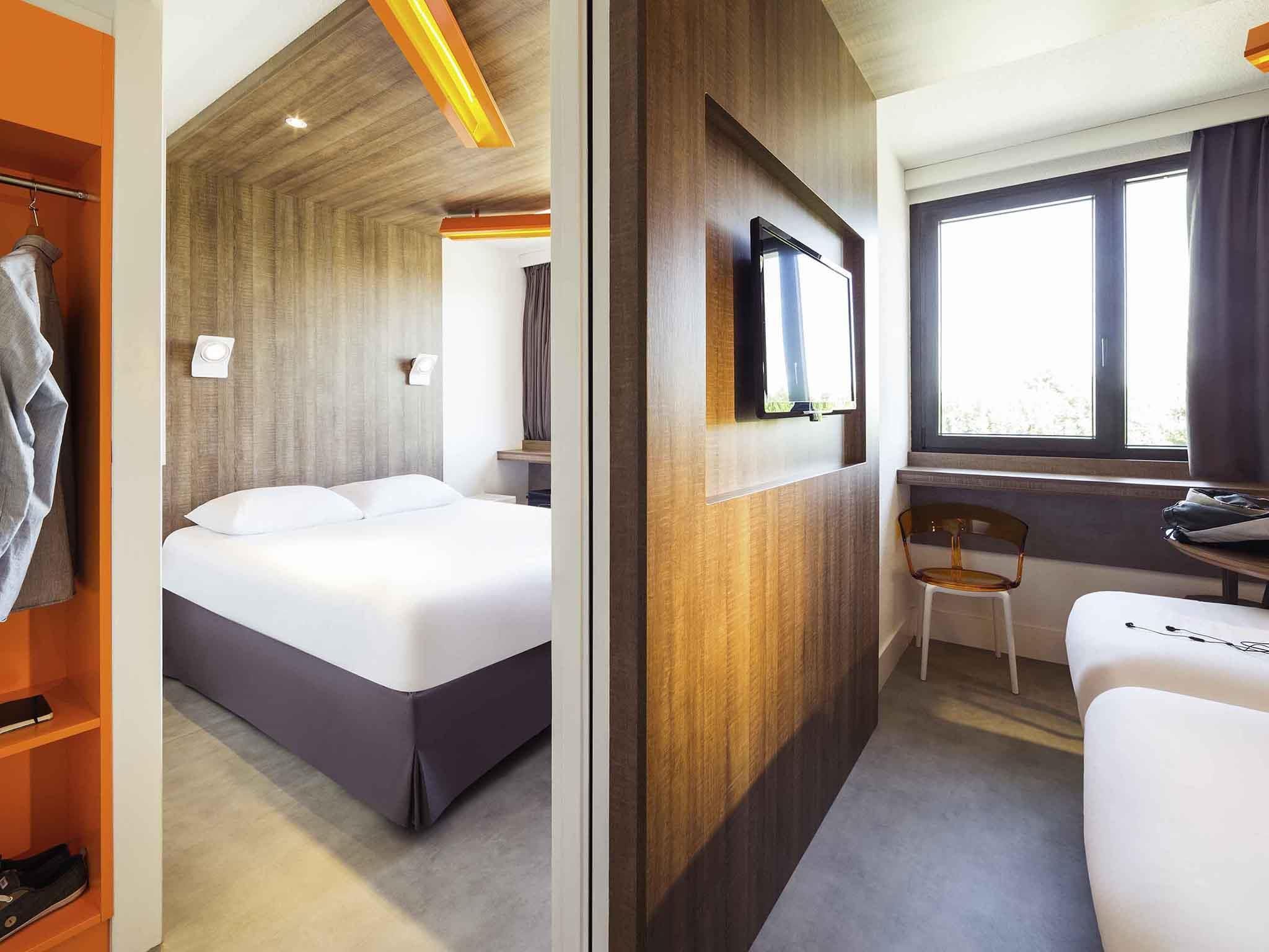 A hotel room with a bed, a desk with a chair, a television, and a window.