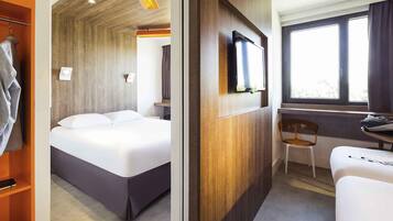 A hotel room with a bed, a desk with a chair, a television, and a window.