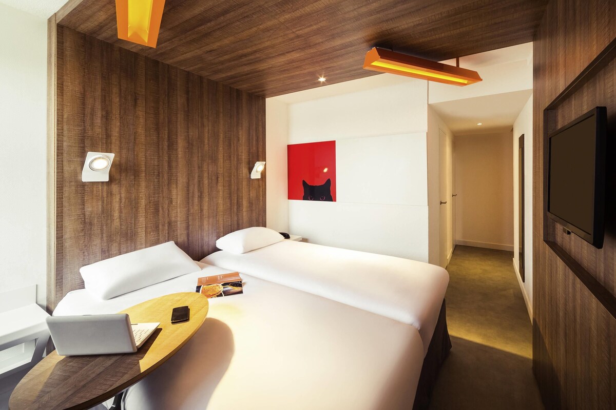 Een moderne hotelkamer met een groot bed, een bureau met een laptop, een flatscreen-televisie en een abstract schilderij in rode tinten aan de muur.