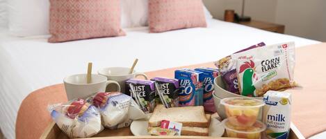A breakfast tray with cereal, milk, and toast on a bed.