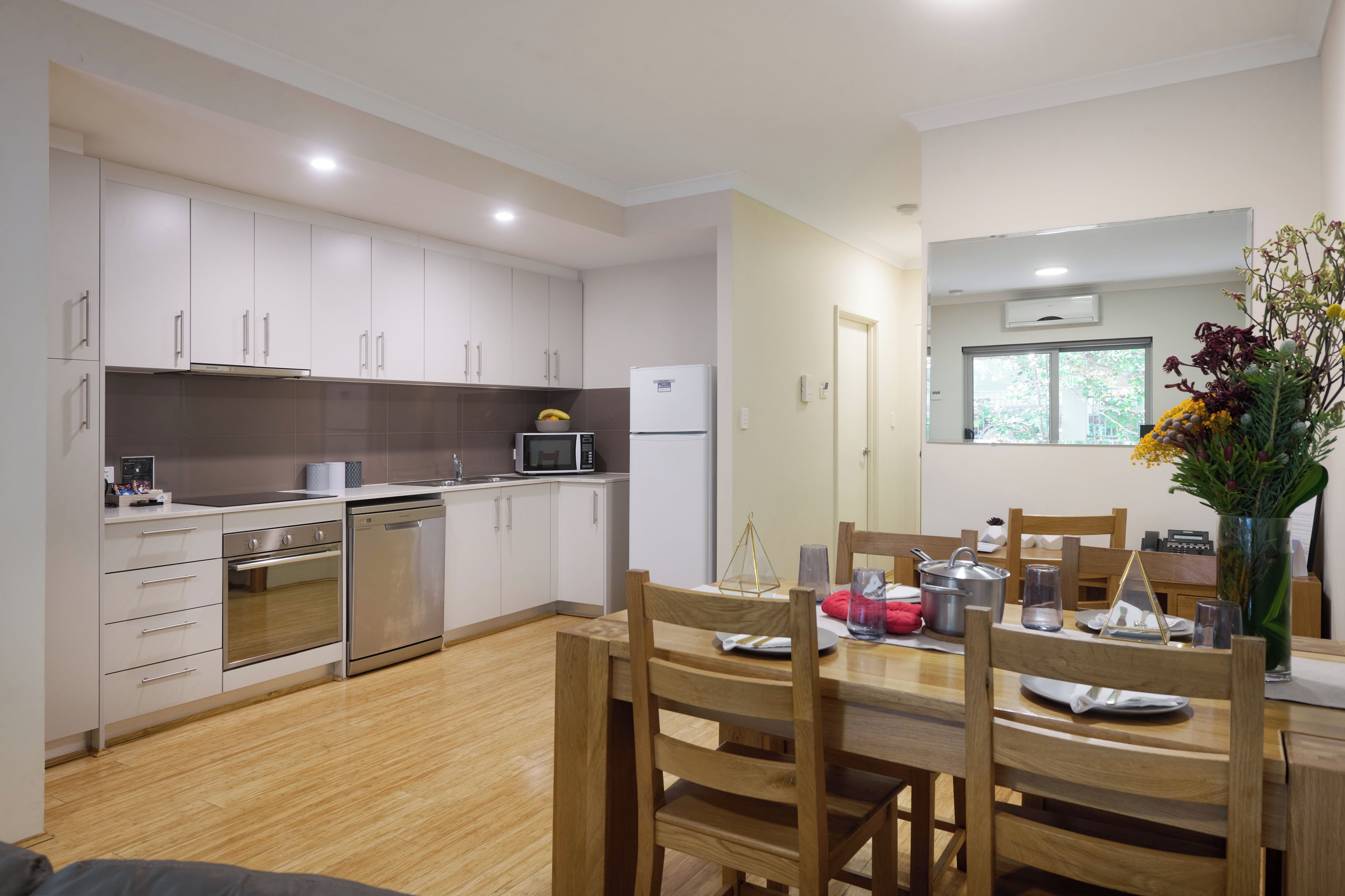 Una cocina moderna con armarios blancos, electrodomésticos de acero inoxidable y una zona de comedor con sillas de madera y una mesa.