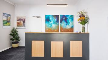 A reception desk with two abstract paintings, a potted plant, and a vase with flowers.