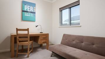 A room with a wooden desk, a brown sofa, a window with a view of solar panels, and a blue wall with text.