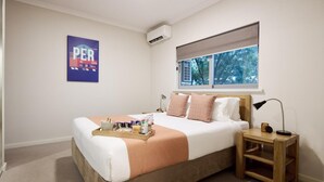 A bedroom with a bed, a bedside table, a nightstand, a window with a view, and a poster on the wall. - Airport Apartments by Vetroblu (Redcliffe)