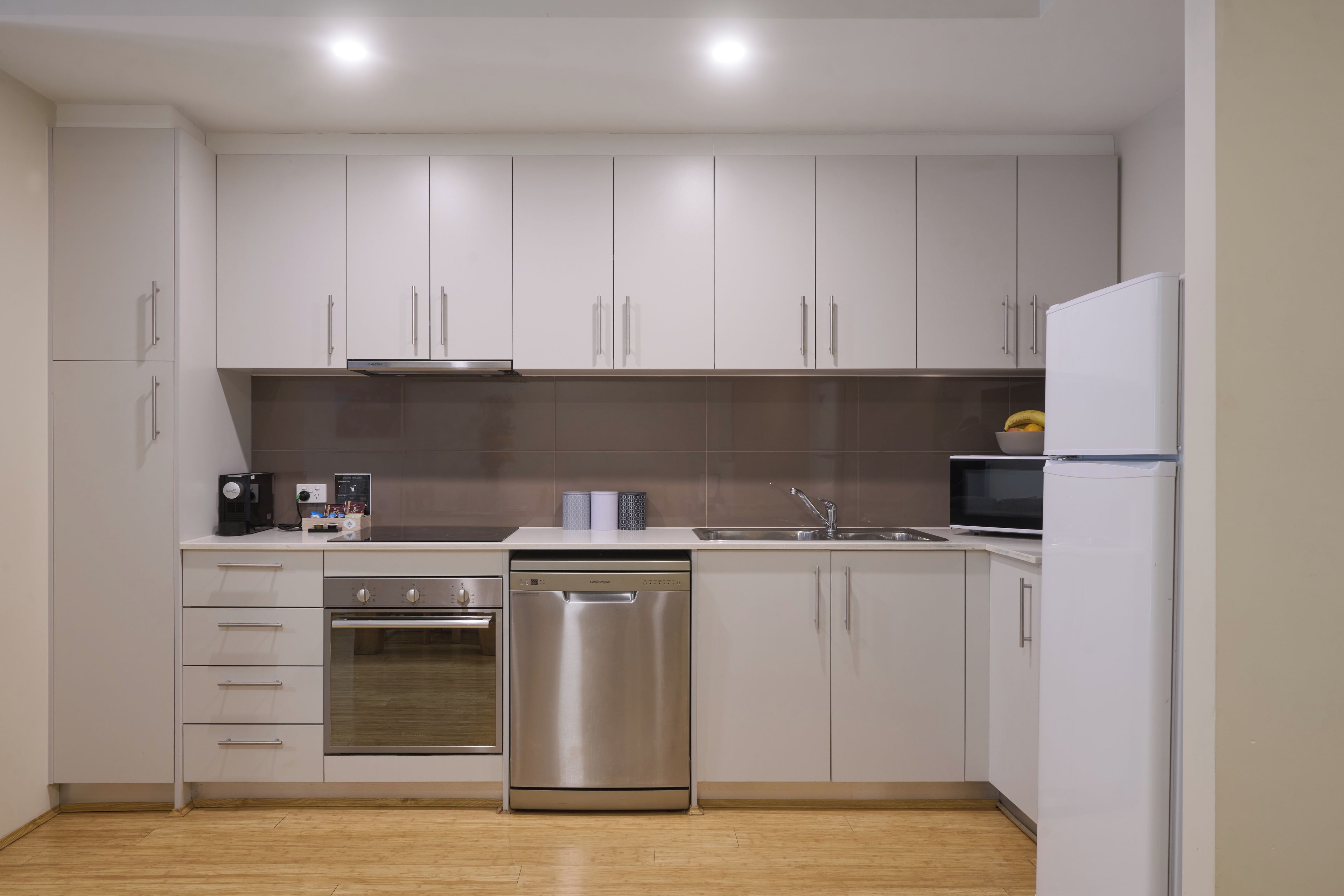 Une cuisine moderne dotée d’appareils électroménagers en acier inoxydable, de meubles blancs et d’un plancher en bois.
