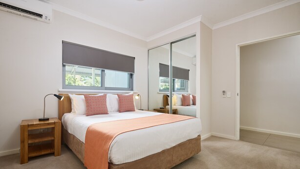 A bedroom with a bed, bedside tables, a window with blinds, a mirror, and a door. - Airport Apartments by Vetroblu (Redcliffe)