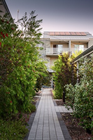 A pathway flanked by lush greenery leading to a modern building with balconies and a solar panel roof. - Airport Apartments by Vetroblu (Redcliffe)