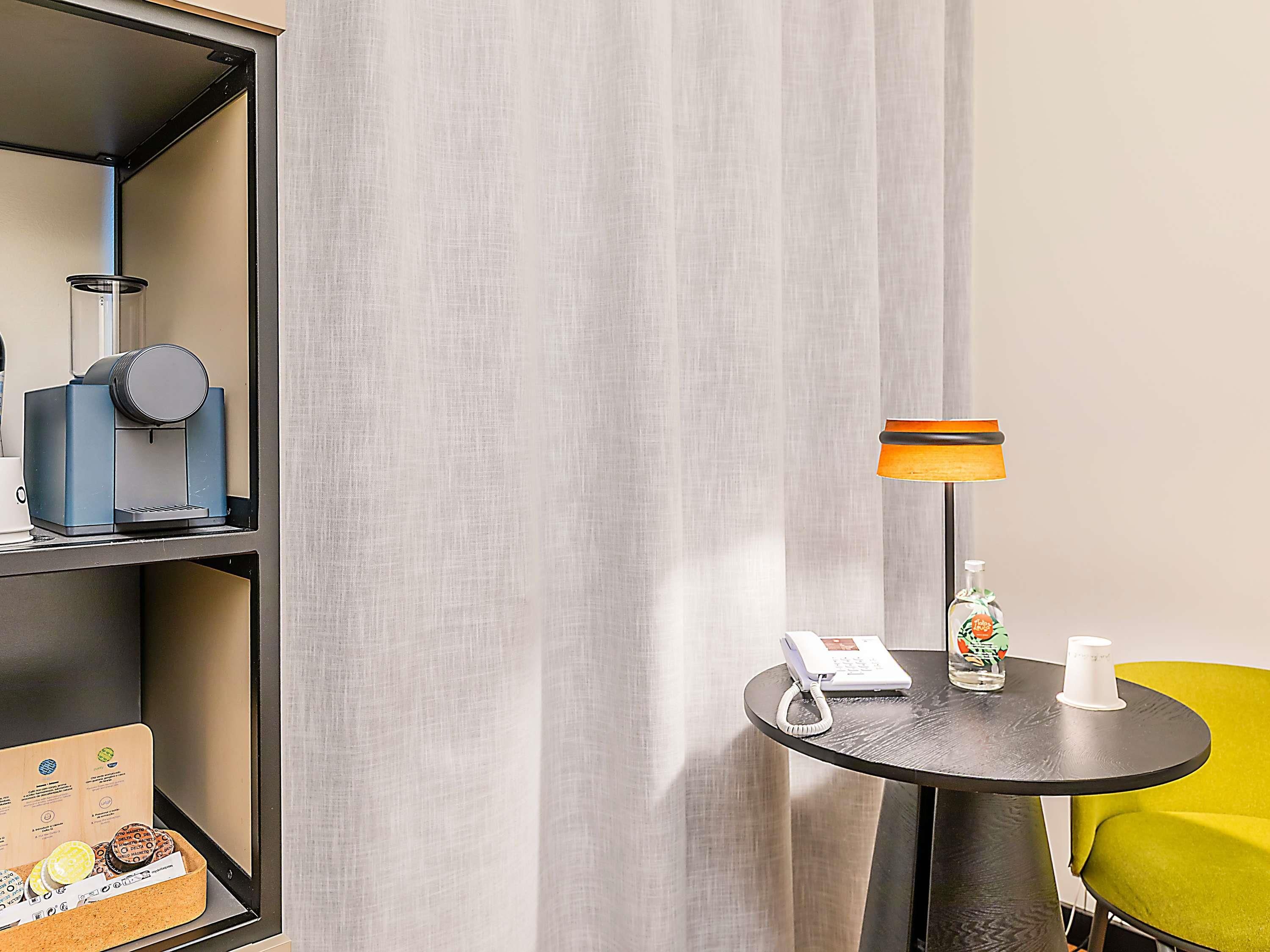 Habitación de hotel con cafetera, teléfono, dispensador de gel hidroalcohólico y una mesita con lámpara.