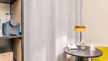 Habitación de hotel con cafetera, teléfono, dispensador de gel hidroalcohólico y una mesita con lámpara.