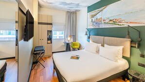Een hotelkamer met een bed, een stoel, een bureau, een televisie en een schilderij aan de muur.