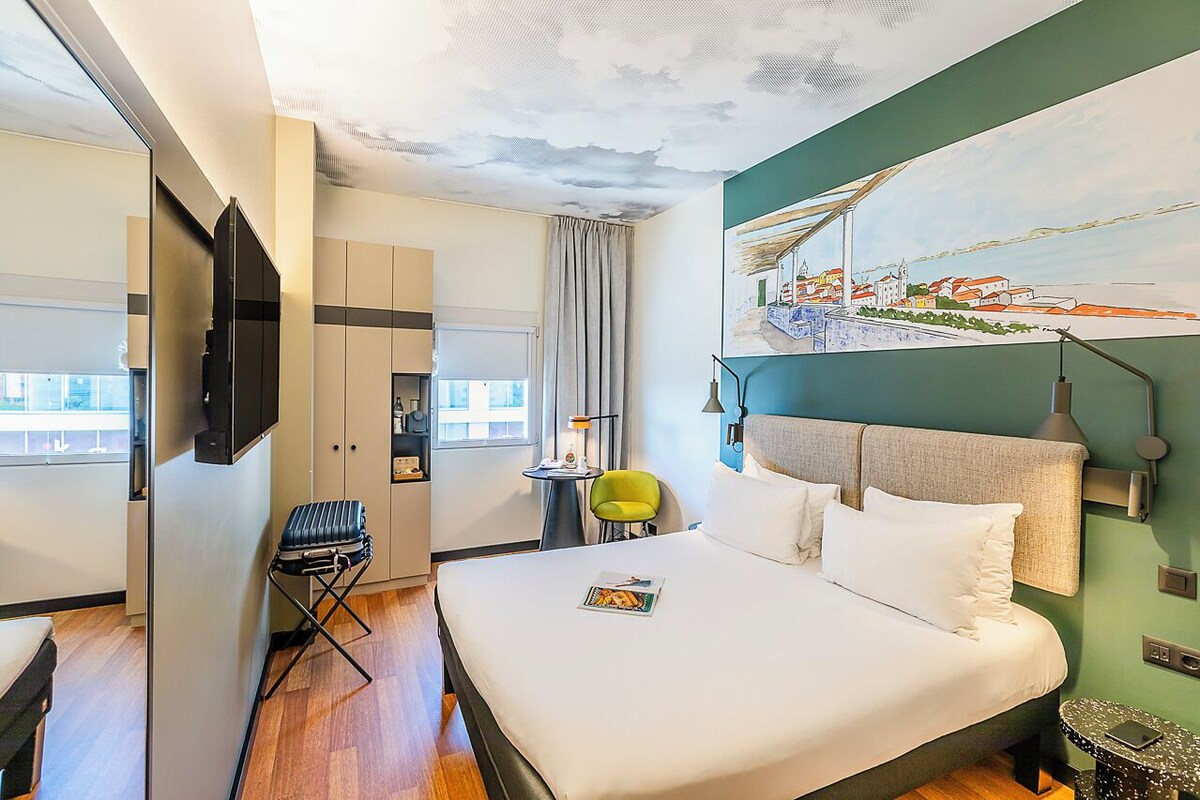 Een hotelkamer met een bed, een stoel, een bureau, een televisie en een schilderij aan de muur.