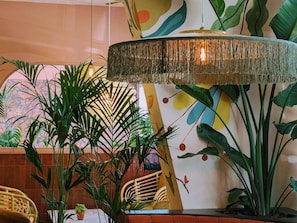 Una habitación con una lámpara colgante grande, un sillón de mimbre y varias plantas en macetas.