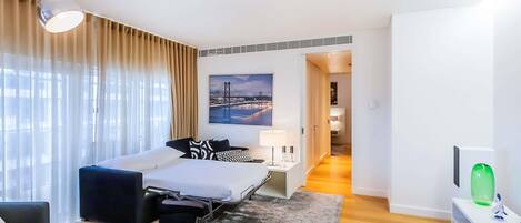 A modern hotel room with a bed, a desk, a chair, a TV, and a painting of a bridge.